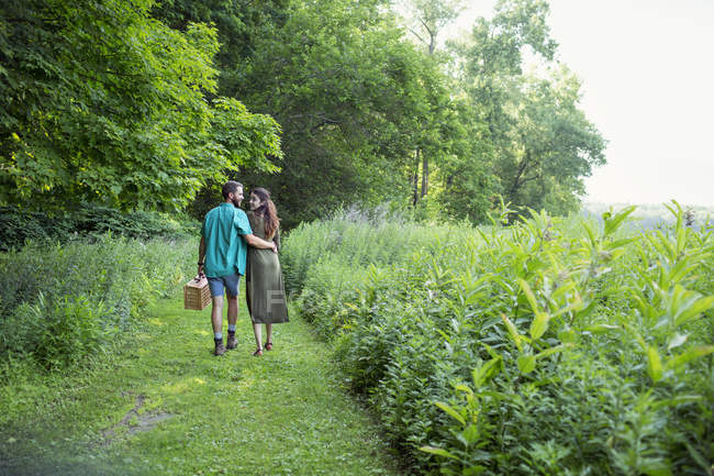 Uomo e donna che camminano attraverso l'erba prato e portando cestino da picnic . — Foto stock