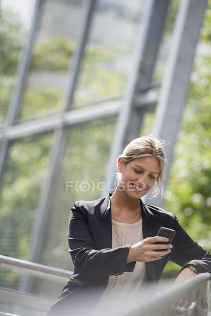 Joven empresaria con chaqueta negra usando smartphone en la ciudad . - foto de stock