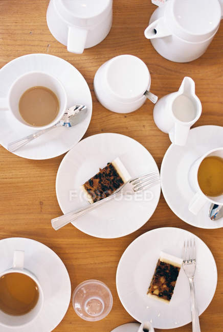 Top view of table set with cups of tea, milk jugs and slices of fruit cake on plates. — Stock Photo