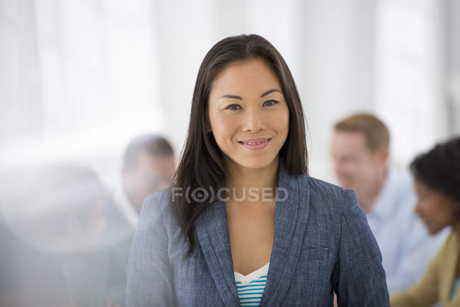 Впевнена бізнес-леді стоїть в кімнаті переговорів з колегами на задньому плані . — стокове фото