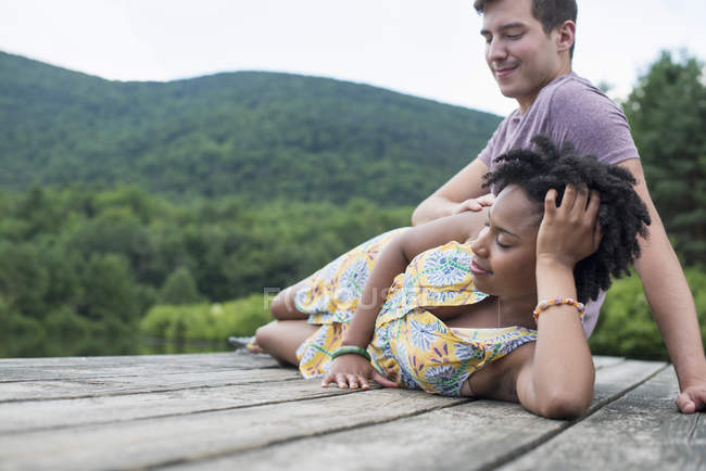 Junges Paar entspannt auf Holzsteg mit Blick auf Bergsee. — Stockfoto