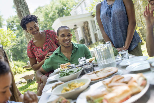 Amici e famiglia si riuniscono intorno al tavolo da pranzo nel giardino di campagna . — Foto stock