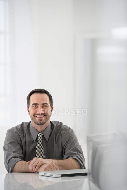 Hombre adulto medio sentado en la mesa al lado de la computadora portátil cerrada . - foto de stock