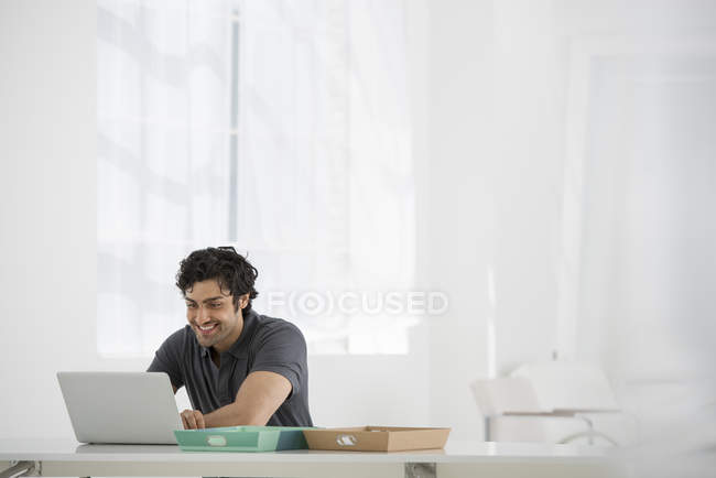 Junger Mann sitzt am Schreibtisch und benutzt Laptop im Büro. — Stockfoto