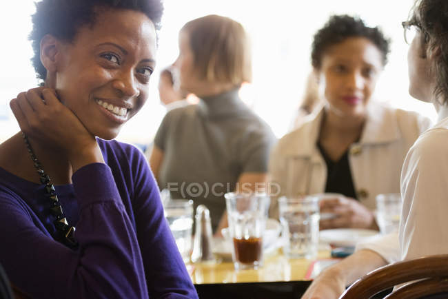 African american woman sitting with hand on chin in bar with friends. — Stock Photo
