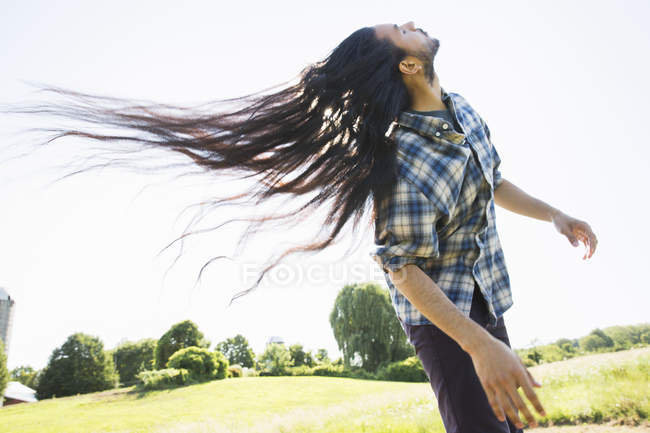 Young man with long dark hair shaking head and fanning on fresh air. — Stock Photo