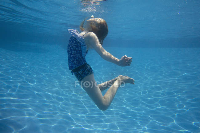 Pre-adolescent girl with fanning long hair swimming underwater in pool. — Stock Photo