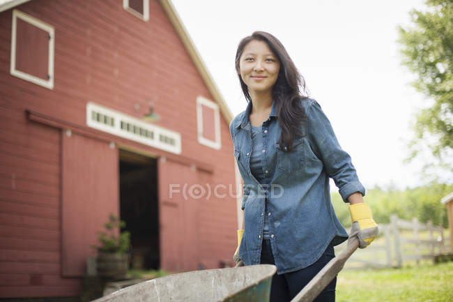 Молодая женщина толкает телегу на ферме в сельской местности — стоковое фото