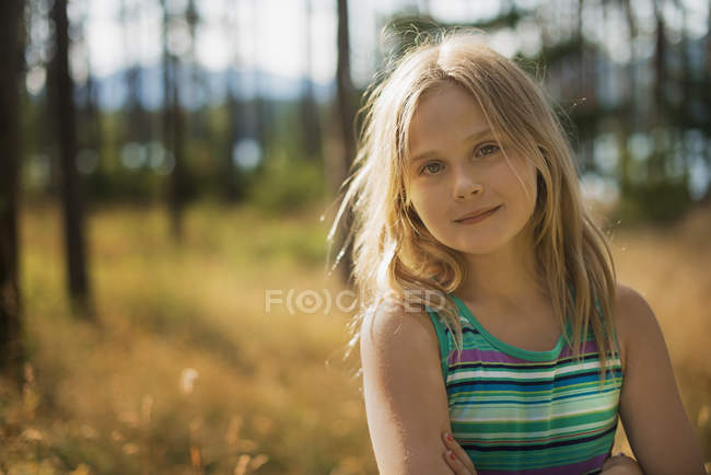 Elementary age girl with long blonde hair in woodland by lake. — Stock Photo