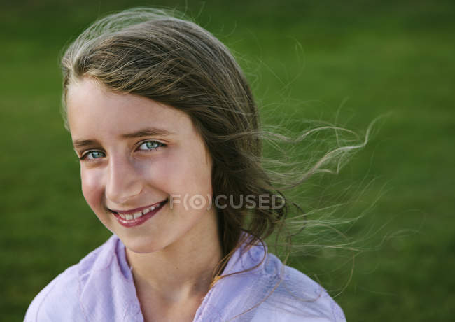 Portrait of smiling elementary age girl against green grass. — Stock Photo