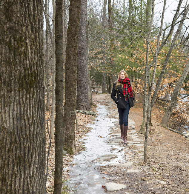 Woman in winter coat and red scarf walking down path in wintry forest. — Stock Photo