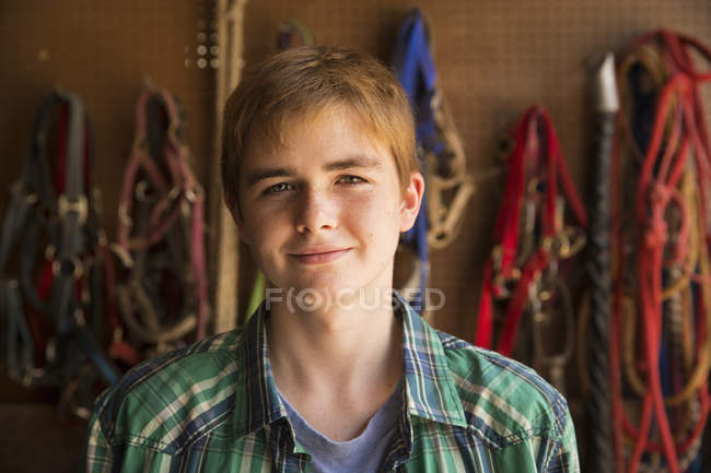 Teenage boy standing in tack room in farmhouse stable. — Stock Photo