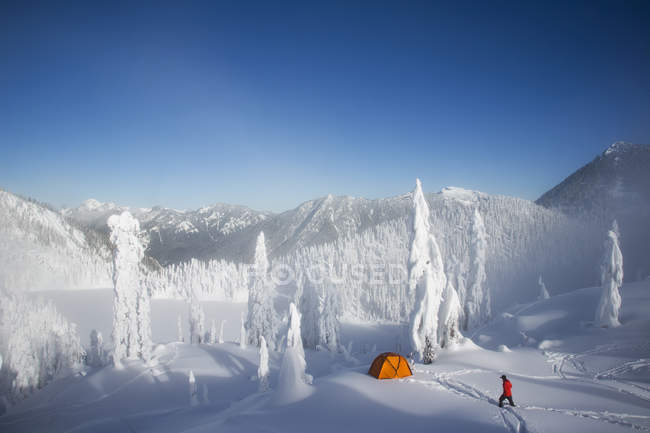 Homme marchant vers une tente orange dans le paysage des Cascades enneigées aux États-Unis . — Photo de stock