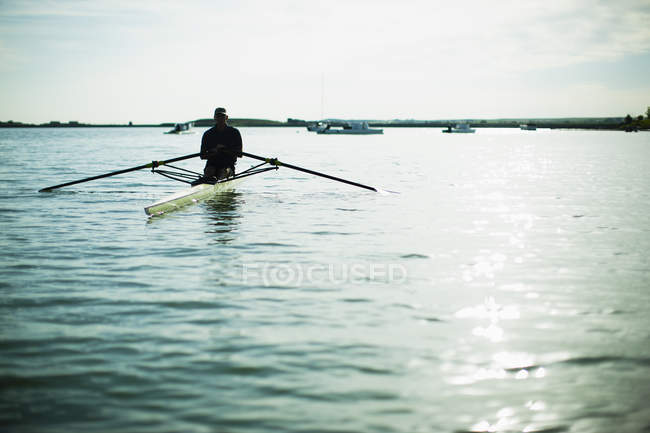 Rear view of man in rowing boat on lake water. — Stock Photo