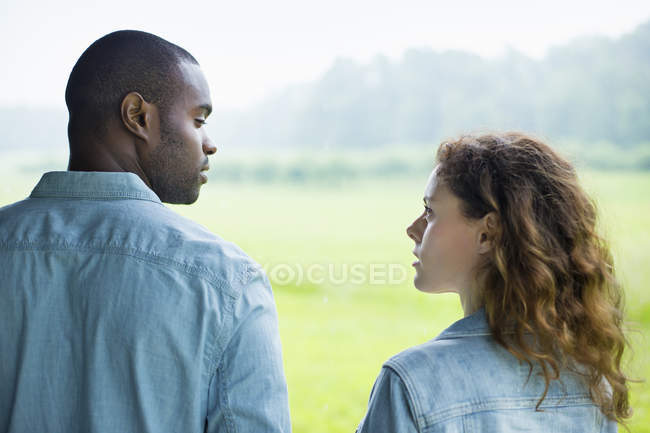 Casal jovem de pé lado a lado no campo verde e olhando um para o outro . — Fotografia de Stock