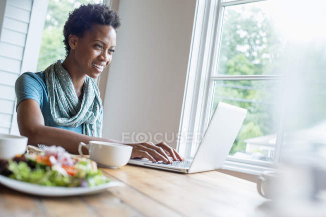 Woman using laptop in cafe with cup of coffee and meal. — Stock Photo