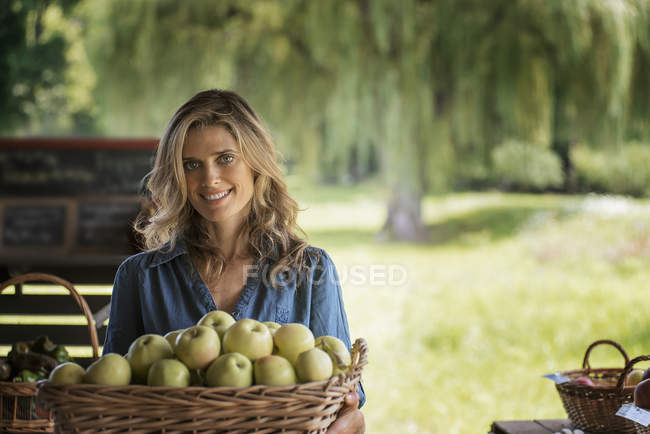 Young woman holding basket of green apples at organic farm. — Stock Photo