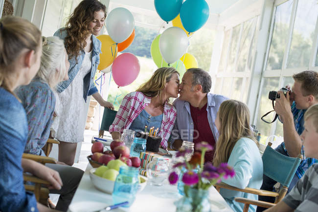 Family gathered around chocolate cake at table on farmhouse terrace. — Stock Photo
