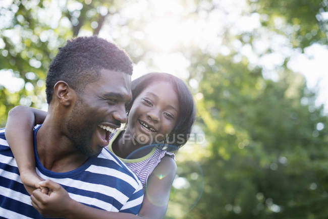 Hombre dando hija a cuestas en la sombra de los árboles en el bosque . - foto de stock