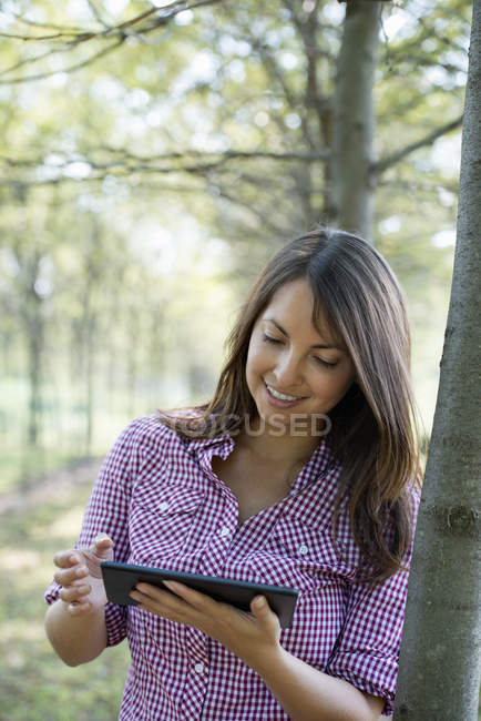 Frau steht in Baumallee und nutzt digitales Tablet. — Stockfoto