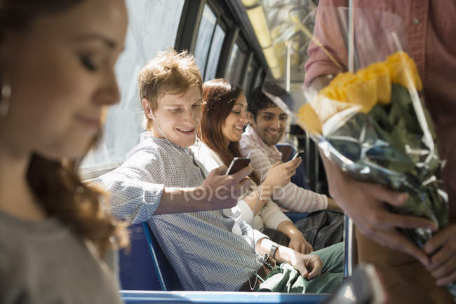 Groupe de personnes en bus urbain avec smartphones et fleurs . — Photo de stock