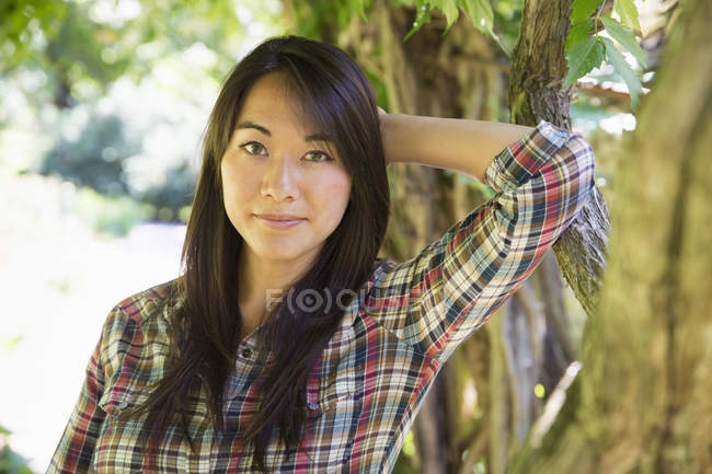 Portrait of  young woman in plaid shirt against tree trunk. — Stock Photo