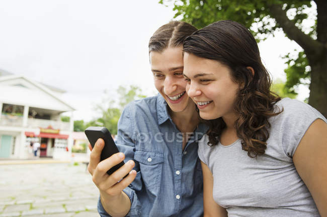 Jovem casal sentado lado a lado e usando smartphone . — Fotografia de Stock