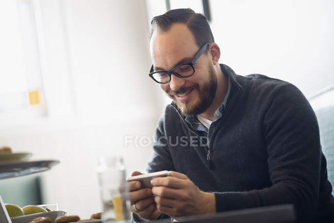 Бородатий чоловік використовує смартфон і посміхається в кафе . — стокове фото