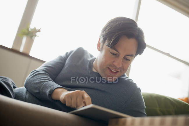 Homem em casa usando tablet digital no sofá . — Fotografia de Stock