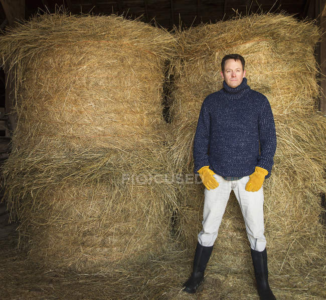 Мужчина позирует на ферме перед стопкой сена . — стоковое фото