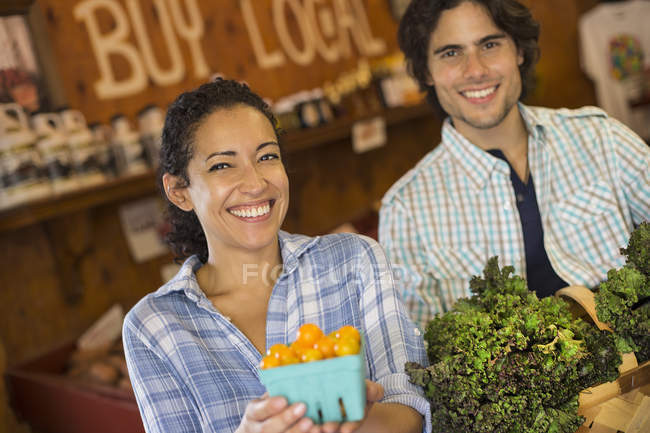 Due persone con cesto di pomodori e verdure a foglia verde riccia nel negozio di fattoria biologica . — Foto stock