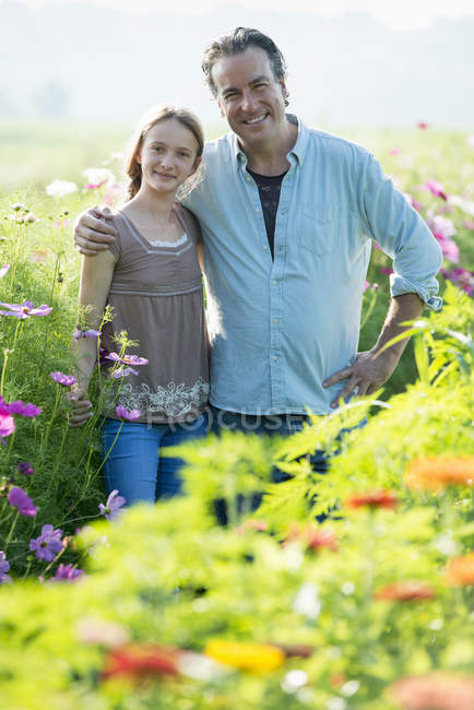 Mature man with daughter posing in green field of flowers. — Stock Photo