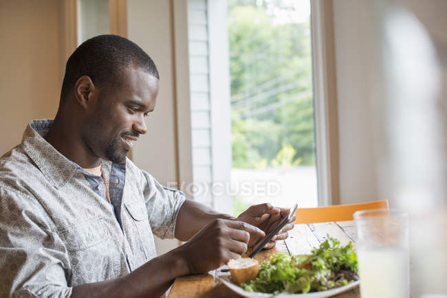 Young man sitting using smartphone in cafe at table with plate of salad. — Stock Photo