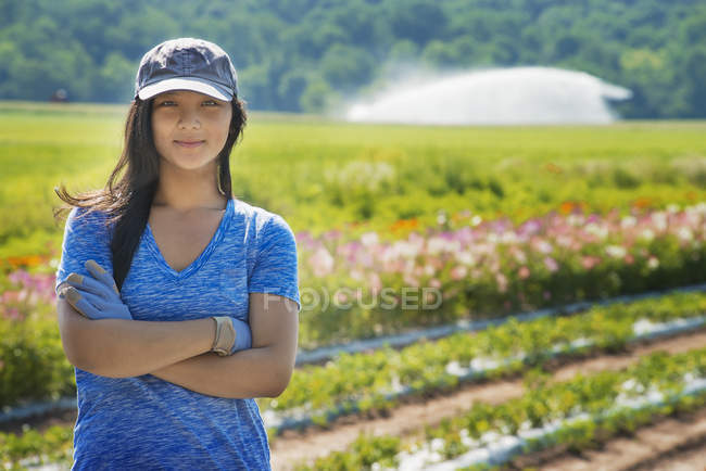 Donna con le braccia incrociate in piedi in campo di colture orticole e fiori . — Foto stock