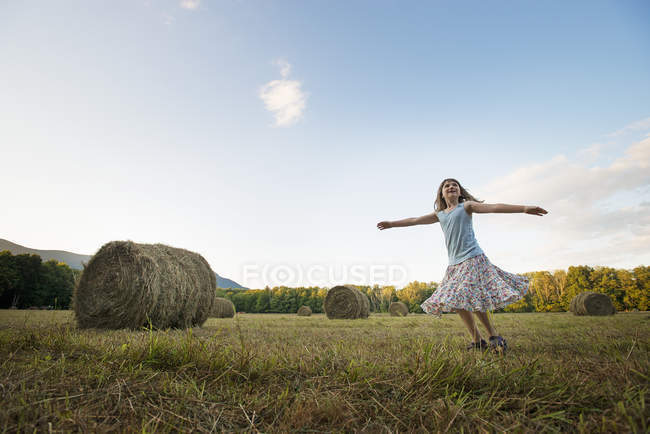 Девушка младшего возраста в платье танцует с распростертыми руками на соломенном поле . — стоковое фото