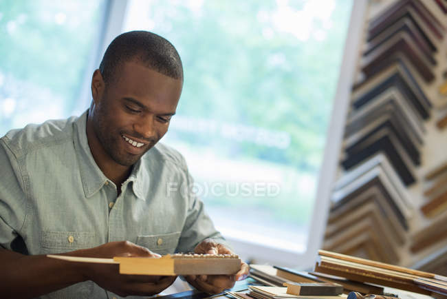 Young man holding picture frame at workbench in picture framing studio. — Stock Photo