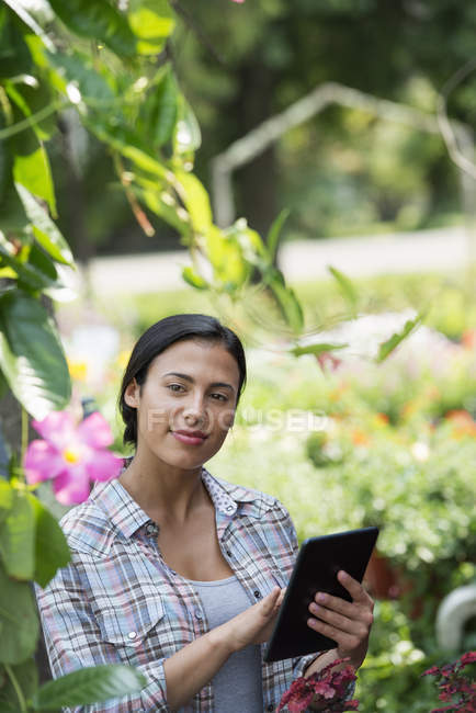Young woman in organic nursery greenhouse using digital tablet. — Stock Photo