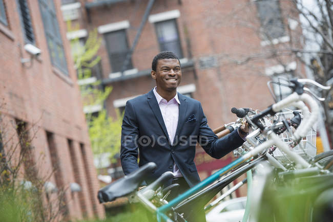 Hombre de traje azul de pie junto al estante de bicicletas en el parque de la ciudad . - foto de stock