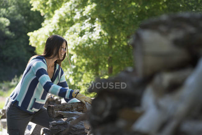 Молода жінка з довгим чорним волоссям укладає колоди в сільській місцевості . — стокове фото