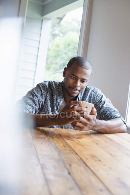 Mann checkt Smartphone an Holztisch im Haus. — Stockfoto