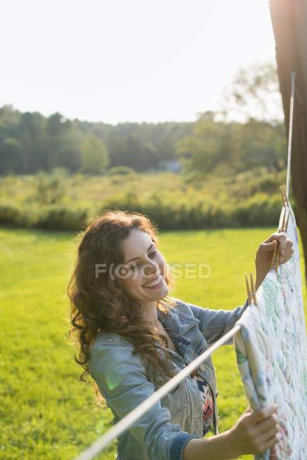 Young woman hanging laundry on washing line in countryside. — Stock Photo