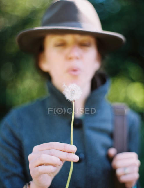 Mulher soprando cabeça de semente de dente de leão ao ar livre . — Fotografia de Stock