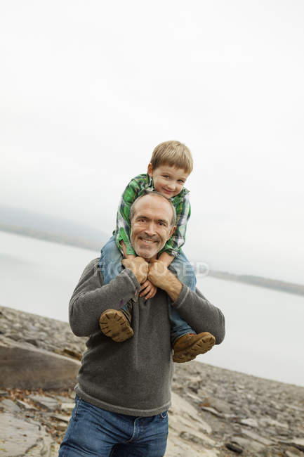 Älterer Mann gibt Kind Huckepackfahrt am Ufer des Sees. — Stockfoto
