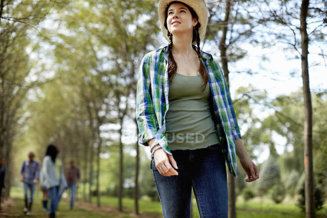 Молода жінка в солом'яному капелюсі, що йде в лісі з друзями на задньому плані . — стокове фото