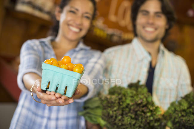 Двоє людей з кошиком помідорів і кучерявими зеленими листовими овочами в органічному фермерському магазині . — стокове фото