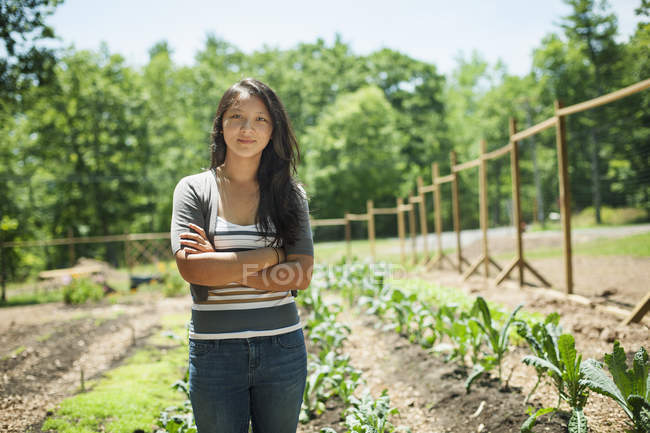 Mujer joven de pie con los brazos cruzados en la granja tradicional en el campo - foto de stock