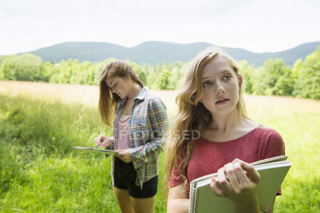 Dos chicas adolescentes de pie sobre hierba verde y dibujando en cuadernos de dibujo . - foto de stock