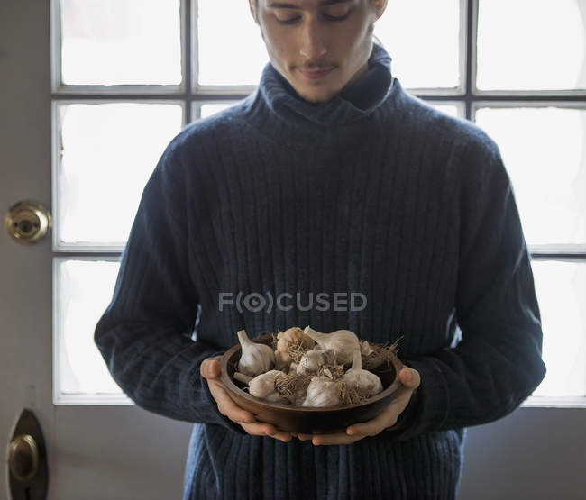 Молодой человек держит миску луковиц чеснока . — стоковое фото