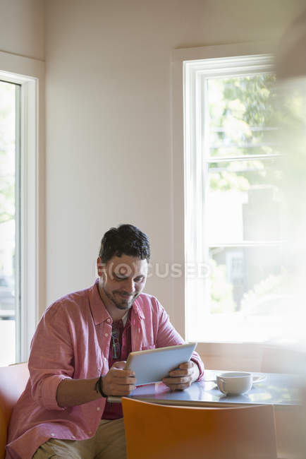 Чоловік сидить за столом кафе і використовує цифровий планшет . — стокове фото