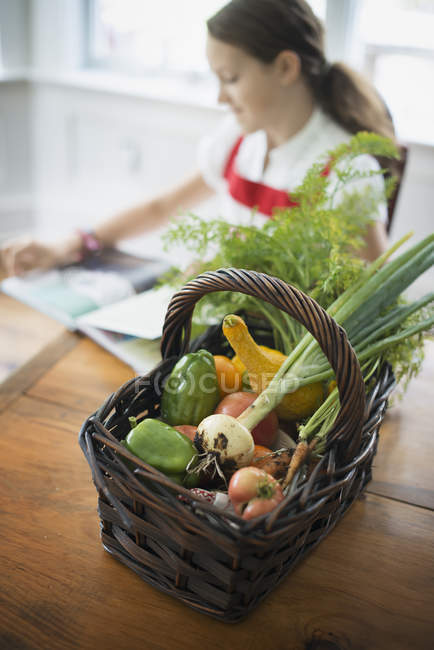 Cesto di verdure fresche di fattoria con ragazza che legge in cucina . — Foto stock